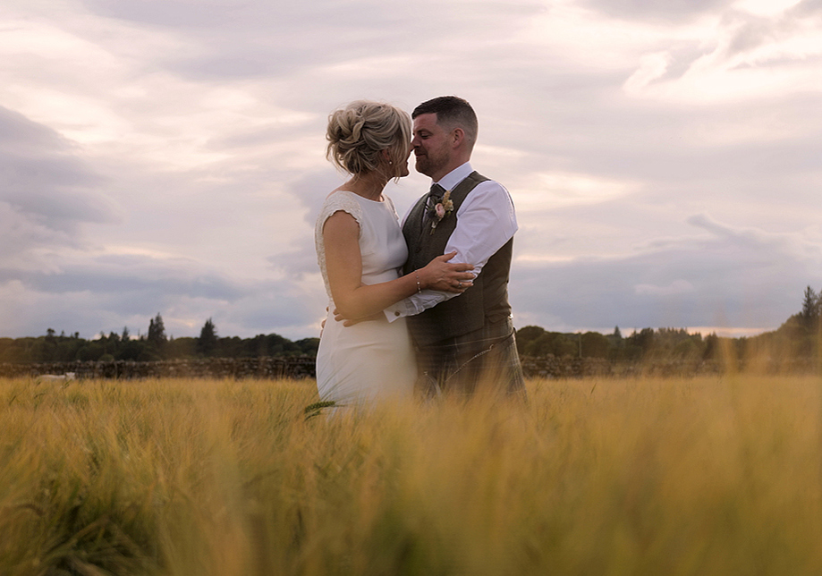 Bride and groom embrace among long grass